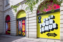 Large-scale yellow and red window vinyl graphics for the Über Tourismus exhibition on the facade of the Architekturzentrum Wien AzW designed by LWZ Studio. LWZ Design and Animation Vienna