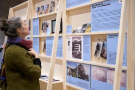 A visitor exploring the Toourism exhibition. Graphic design by LWZ Studio, featuring light wooden display structures, blue information panels and historical photography at Architekturzentrum Wien. LWZ Design and Animation Vienna
