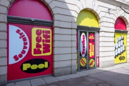 Vibrant red and yellow graphic design window vinyls by LWZ Studio for the Toourism exhibition, featuring bold typography stickers on the historic courtyard windows of Architekturzentrum Wien. LWZ Design and Animation Vienna